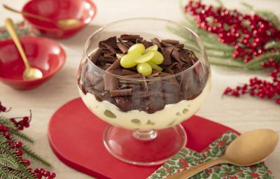 Fotografia mostra uma taça de sobremesa transparente com uma camada de creme branco com uvas. Por cima uma ganache de chocolate, com raspas de chocolate e pedaços de uva para decorar.