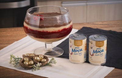 À esquerda, uma taça grande de bombom de framboesa, tendo três camadas; à direita, duas latas de leite condensado lado a lado