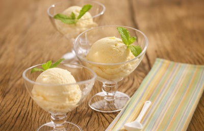 Em uma mesa de madeira contém duas taças de vidro com uma bola de sorvete cada.