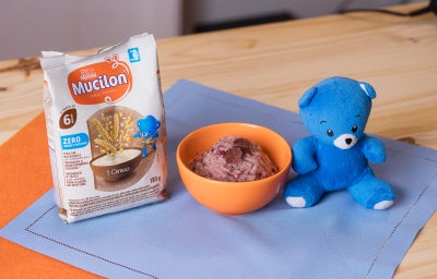 Fotografia em tons de laranja e azul em uma bancada de madeira com paninhos azuis. Ao centro, um bowl laranja com sorvete de uva dentro.