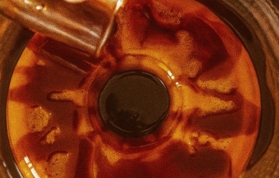 Fotografia vista de cima de um flan com uma calda de chocolate sendo despejada por cima.