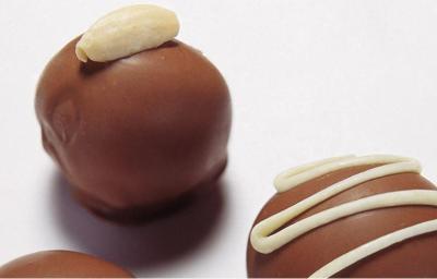 fotografia em tons de branco e marrom de uma bancada branca vista de cima que contém 3 bombons de chocolate fotografia em tons de branco e marrom de uma bancada branca vista de cima que contém 3 bombons de chocolate