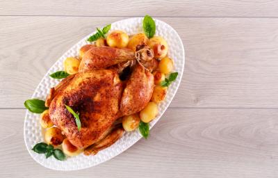 fotografia em tons de cinza, branco e bege de uma bancada cinza vista de cima. Contém um recipiente oval branco com frango assado e batatas bolinhas ao redor. fotografia em tons de cinza, branco e bege de uma bancada cinza vista de cima. Contém um recipiente oval branco com frango assado e batatas bolinhas ao redor.