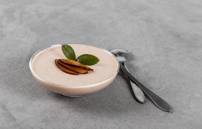 Fotografia em tons de branco em uma bancada de madeira de cor cinza. Ao centro, uma taça contendo a mousse com duas colheres ao lado. Fotografia em tons de branco em uma bancada de madeira de cor cinza. Ao centro, uma taça contendo a mousse com duas colheres ao lado.