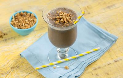 Foto de uma bancada de madeira amarelada. Sobre ela há um pano azul claro no qual está apoiada uma taça com a bebida de açaí, decorada. Há na taça um canudo de papel amarelo e branco, outro na mesa e, ao fundo, um recipiente com granola Foto de uma bancada de madeira amarelada. Sobre ela há um pano azul claro no qual está apoiada uma taça com a bebida de açaí, decorada. Há na taça um canudo de papel amarelo e branco, outro na mesa e, ao fundo, um recipiente com granola