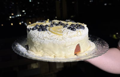 imagem mostra um bolo de massa clara com pontinhos roxos e um creme aveludado branco por cima