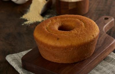 Foto aproximada do bolo de milho com erva-doce, redondo, com furo central, bem dourado, sobre uma tábua de madeira com um punhado de fubá aparecendo ao fundo Foto aproximada do bolo de milho com erva-doce, redondo, com furo central, bem dourado, sobre uma tábua de madeira com um punhado de fubá aparecendo ao fundo