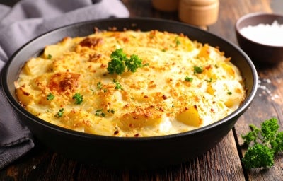 Em cima de uma mesa, refratário redondo com molho cremoso e queijo gratinado, decoado com florete de brocólis. Em cima de uma mesa, refratário redondo com molho cremoso e queijo gratinado, decoado com florete de brocólis.