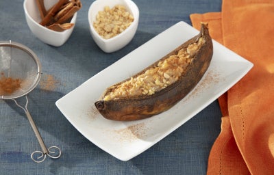 Fotografia em tons de laranja com um prato branco ao centro. Em cima do prato existe uma receita de banana assada coberta com pedaços de amendoim e polvilhada com canela Fotografia em tons de laranja com um prato branco ao centro. Em cima do prato existe uma receita de banana assada coberta com pedaços de amendoim e polvilhada com canela