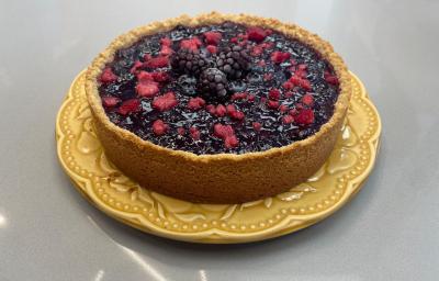 Foto da receita de torta ridícula servida em uma porção grande decorada com frutas vermelhas em cima. Torta está sobre um prato amarelo em cima de uma bancada cinza