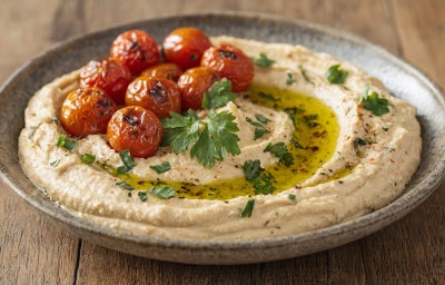 Fotografia em tons claros com uma pasta feita de couve flor e ricota ao centro. Em cima da pasta existe tomates e salsinha