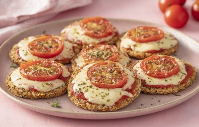 Imagem mostra uma pizza pequena com uma base verde e queijo gratinado por cima com rodelas de tomate e folhas de manjericão