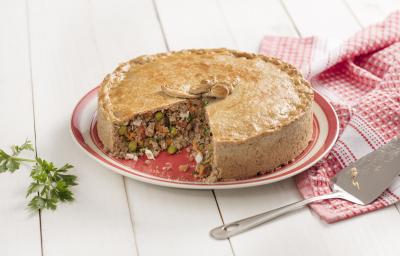 Fotografia em tons de branco, dourado e vermelho, com torta de carne assada e fatiada sobre prato vermelho e branco, ao lado guardanapo em branco e vermelho e uma espátula, ramo de salsa ao lado esquerdo, tudo sobre bancada de madeira na cor branca. Fotografia em tons de branco, dourado e vermelho, com torta de carne assada e fatiada sobre prato vermelho e branco, ao lado guardanapo em branco e vermelho e uma espátula, ramo de salsa ao lado esquerdo, tudo sobre bancada de madeira na cor branca.