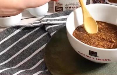 Foto da receita de Brigadeiro Plant-based. Observa-se uma tigela branca com o brigadeiro de colher dentro e as embalagens de Natures Heart atrás.