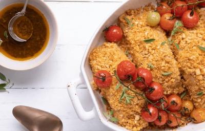 Fotografia em tons de amarelo em uma bancada de madeira branca com um refratário oval branco com as postas de bacalhau com crosta de pão e tomatinhos cereja assados dentro dele. Fotografia em tons de amarelo em uma bancada de madeira branca com um refratário oval branco com as postas de bacalhau com crosta de pão e tomatinhos cereja assados dentro dele.