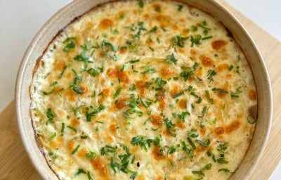 Visto de cima, prato de porcelana bege com queijo gratinado, decorado com cheiro-verde picado.