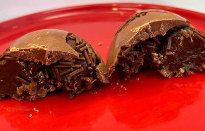 Na imagem duas cascas de ovo de pascoa de chocolate recheadas com brigadeiro em tons marrom e castanha. As cascas estão sobre um prato vermelho que preenche todo o restante da imagem.
