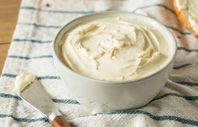Fotografia mostra um requeijão servido em um pote branco sobre um pano listrado.