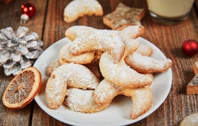 Em cima de uma mesa, prato branco com biscoitos em forma de meia lua, polvilhados com açúcar de confeiteiro. Em cima de uma mesa, prato branco com biscoitos em forma de meia lua, polvilhados com açúcar de confeiteiro.