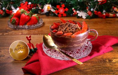 Fotografia em tons de vermelho em uma bancada de madeira, um pano vermelho com uma taça de vidro e o pavê de chocolate Alpino com morangos dentro dela. Ao lado, uma colher dourada e uma cápsula de Dolce Gusto Alpino. Ao fundo, decoração natalina. Fotografia em tons de vermelho em uma bancada de madeira, um pano vermelho com uma taça de vidro e o pavê de chocolate Alpino com morangos dentro dela. Ao lado, uma colher dourada e uma cápsula de Dolce Gusto Alpino. Ao fundo, decoração natalina.
