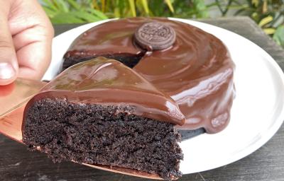 Foto aproximada de um bolo de chocolate com a fatia na frente sobre uma faca. O bolo está decorado com uma calda de chocolate e com um biscoito Negresco no centro. Foto aproximada de um bolo de chocolate com a fatia na frente sobre uma faca. O bolo está decorado com uma calda de chocolate e com um biscoito Negresco no centro.