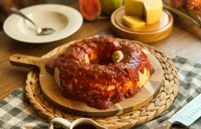 Fotografia de um pudim de queijo colonial com calda de goiabada sobre uma tábua de madeira redonda. Ao fundo tem um prato branco fundo, colher de sopa e mini tábua grossa de madeira com o queijo colonial cortado. Fotografia de um pudim de queijo colonial com calda de goiabada sobre uma tábua de madeira redonda. Ao fundo tem um prato branco fundo, colher de sopa e mini tábua grossa de madeira com o queijo colonial cortado.