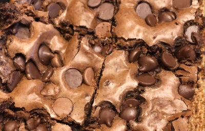 Brownie de chocolate cortado em quadrados, com gotas de chocolate na superfície e casquinha crocante.