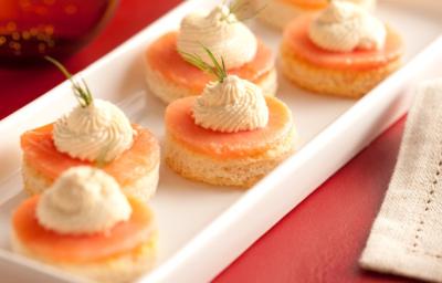 Fotografia em tons de vermelho em uma bancada de madeira com um jogo americano vermelho, um recipiente branco retangular com alguns canapés de salmão em cima dele. Fotografia em tons de vermelho em uma bancada de madeira com um jogo americano vermelho, um recipiente branco retangular com alguns canapés de salmão em cima dele.