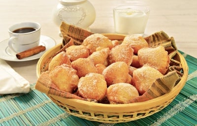 Em cima de uma mesa, cesta de palha com pano listrado com bolinhos de chuva, polvilhado com açúcar de confeiteiro. Em cima de uma mesa, cesta de palha com pano listrado com bolinhos de chuva, polvilhado com açúcar de confeiteiro.