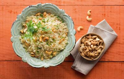 em uma mesa na cor vermelha, contém dois recipientes. Um contém o arroz e o outro as castanhas-de-caju.