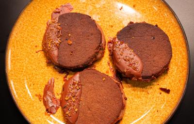 Fotografia em tons de amarelo com um prato amarelo ao centro. Em cima do prato existe uma receita de biscoito de chocolate recheado com sorvete de chocolate. Fotografia em tons de amarelo com um prato amarelo ao centro. Em cima do prato existe uma receita de biscoito de chocolate recheado com sorvete de chocolate.