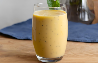 Fotografia de um copo de vidro grande com vitamina de maracujá. No fundo tem um pano azul escuro, que está sobre uma mesa de madeira.