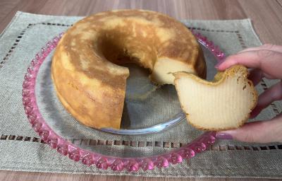 Fotografia de um bolo de farinha láctea sobre um apoio decorativo de vidro raso apoiado em um pano de tom verde.