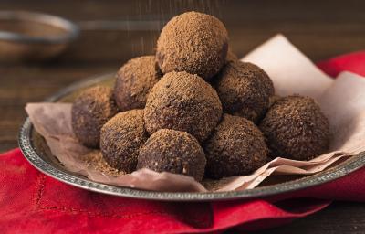 foto em tons de marrom e vermelho de uma bancada marrom vista de frente, contém um pano vermelho, uma bandeja de alumínio com um pano rosa e trufas de chocolate polvilhadas com cacau.