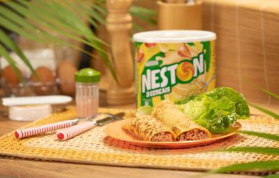 Foto de uma bancada, sobre ela há um jogo americano e nele um prato com dois wraps recheados. Ao fundo há uma lata de Neston 3 Cereais, alguns talheres e outros utensílios. Há algumas plantas compondo a imagem. Foto de uma bancada, sobre ela há um jogo americano e nele um prato com dois wraps recheados. Ao fundo há uma lata de Neston 3 Cereais, alguns talheres e outros utensílios. Há algumas plantas compondo a imagem.