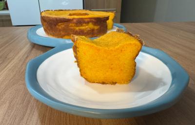 Fotografia em tons claros com um bolo de cenoura mole ao centro. O bolo de cenoura tem cor laranja, textura lisa e cremosa Fotografia em tons claros com um bolo de cenoura mole ao centro. O bolo de cenoura tem cor laranja, textura lisa e cremosa