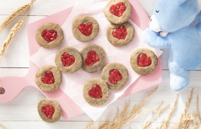 Foto da receita de Biscoitos de Coração. Observa-se uma tábua rosa bebê com os biscoitos dispostos sobe um papel manteiga. Alguns trigos e o ursinho de Mucilon decoram a foto.