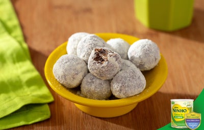 Doces de aveia em formato de bolinhas, cobertos com açúcar, dispostos em prato amarelo sobre mesa de madeira.
