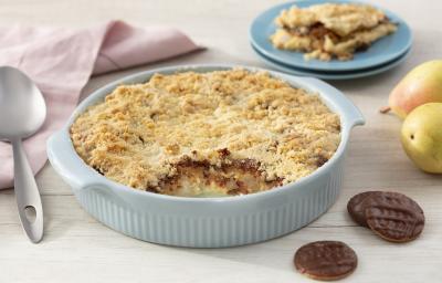 Fotografia em tons de azul em uma bancada de madeira clara, um paninho bege, um recipiente azul claro com o crumble de pera com calipso. Ao fundo, um prato com um pedaço do crumble, peras e calipso espalhados pela mesa. Fotografia em tons de azul em uma bancada de madeira clara, um paninho bege, um recipiente azul claro com o crumble de pera com calipso. Ao fundo, um prato com um pedaço do crumble, peras e calipso espalhados pela mesa.