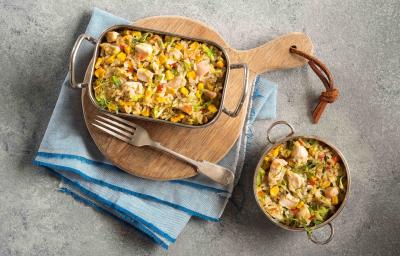 Foto em tons de cinza, azul e marrom uma bancada cinza vista de cima, um pano azul claro, uma tábua de madeira redonda com um recipiente retangular com alças que contém arroz com pedaços de frango, um garfo e um recipiente redondo com arroz e frango Foto em tons de cinza, azul e marrom uma bancada cinza vista de cima, um pano azul claro, uma tábua de madeira redonda com um recipiente retangular com alças que contém arroz com pedaços de frango, um garfo e um recipiente redondo com arroz e frango