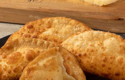 Fotografia de cinco pasteis fritos sobre um prato escuro. Um desses pasteis está aberto, mas sem recheio. Fotografia de cinco pasteis fritos sobre um prato escuro. Um desses pasteis está aberto, mas sem recheio.