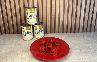 Docinhos de chocolate com granulado vermelho em forminhas vermelhas, dispostos em prato vermelho com Leite Moça ao fundo.