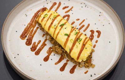 Foto profissional da Receita de Omurice com Arroz Frito e Omelete Cremosa em um prato redondo, decorado com um molho
