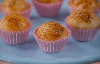 Fotografia de seis unidades de embalagens rosas, uma perto da outra, formando um hexágono. em cada forminha, tem um brigadeiro de creme brulée. As embalagens estão sobre um apoio de cor azul claro. Fotografia de seis unidades de embalagens rosas, uma perto da outra, formando um hexágono. em cada forminha, tem um brigadeiro de creme brulée. As embalagens estão sobre um apoio de cor azul claro.
