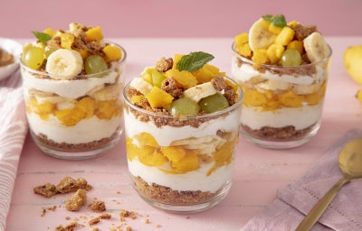 Imagem mostra uma taça de vidro transparente com camada de creme branco, biscoito e frutas