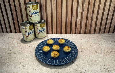 Fotografia em tons de bege em uma bancada, com Leite Moça ao fundo e um prato azul ao centro com brigadeiros