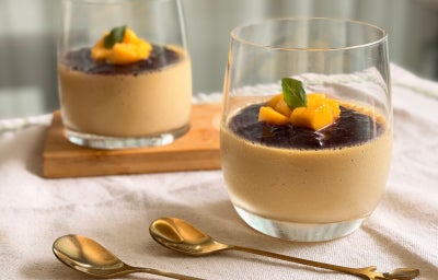 Fotografia mostra dois copos transparentes com creme alaranjado e frutas no topo.