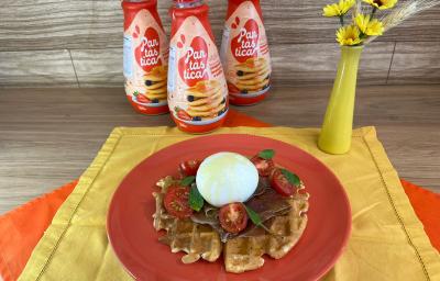 Fotografia em tons de vermelho com um prato vermelho ao centro. Em cima do prato existe uma receita de waffle com burrata, presunto de parma, tomate cereja e manjericão. Ao fundo existe três garrafas de PANTÁSTICA, um produto para fazer panquecas. Fotografia em tons de vermelho com um prato vermelho ao centro. Em cima do prato existe uma receita de waffle com burrata, presunto de parma, tomate cereja e manjericão. Ao fundo existe três garrafas de PANTÁSTICA, um produto para fazer panquecas.