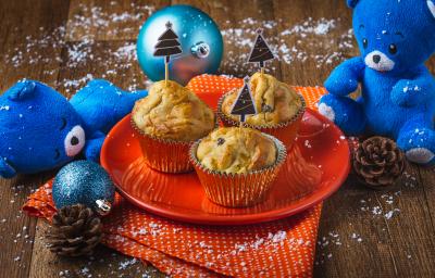 Fotografia em tons de laranja e azul em uma bancada de madeira, um prato laranja com três muffins em cima dele. Ao lado, enfeites e decoração natalina. Fotografia em tons de laranja e azul em uma bancada de madeira, um prato laranja com três muffins em cima dele. Ao lado, enfeites e decoração natalina.