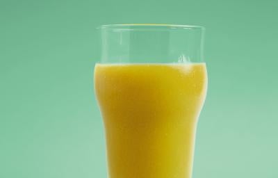 Fotografia em tons de verde em um fundo e bancada verde com um copo de vidro e o suco de manga, limão-siciliano e erva-cidreira dentro dele. Fotografia em tons de verde em um fundo e bancada verde com um copo de vidro e o suco de manga, limão-siciliano e erva-cidreira dentro dele.